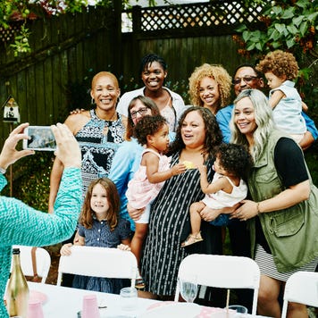 Woman taking photo with smartphone of smiling multi-generation family at backyard birthday party