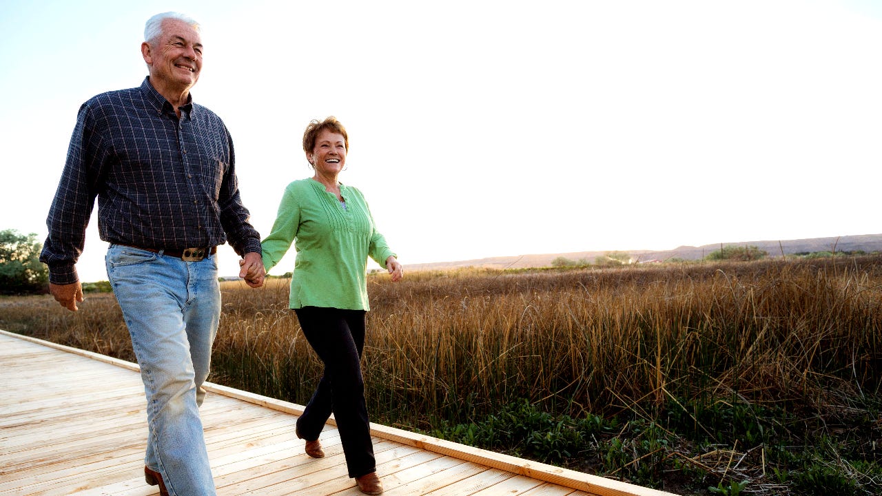 Older white couple walks down boardwalk