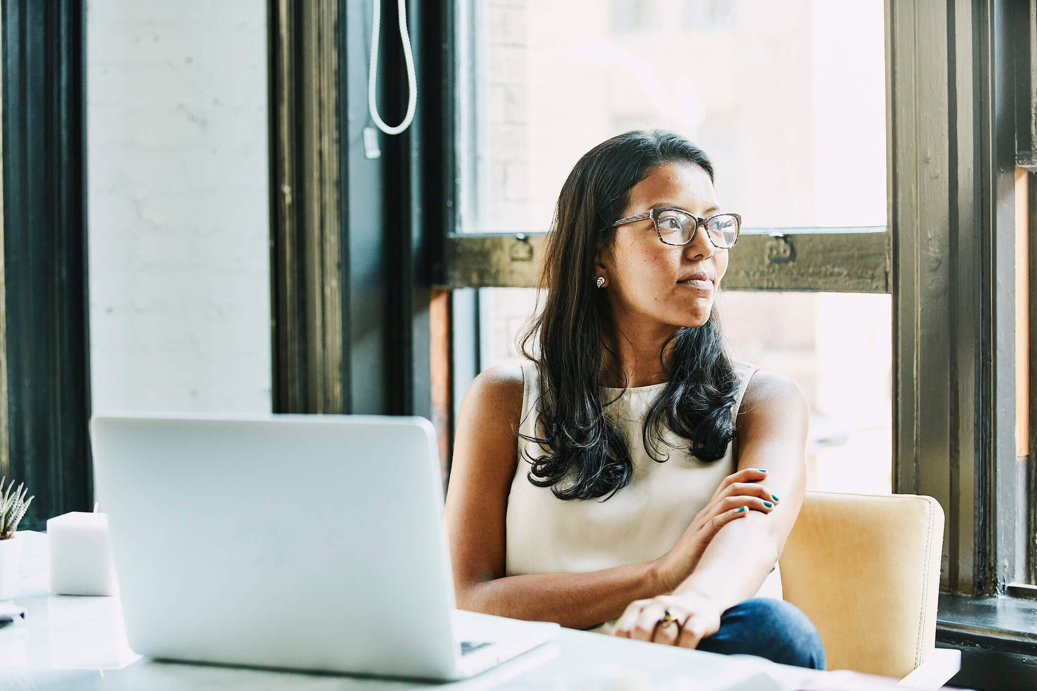 Woman sitting at a table with a laptop in front of her, but she's looking to the right of the photo.
