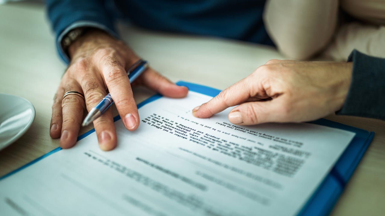 Paper document on table with two individuals' hands showing reviewing the document.