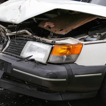 An old white car with the hood bent and crumpled from a collision.