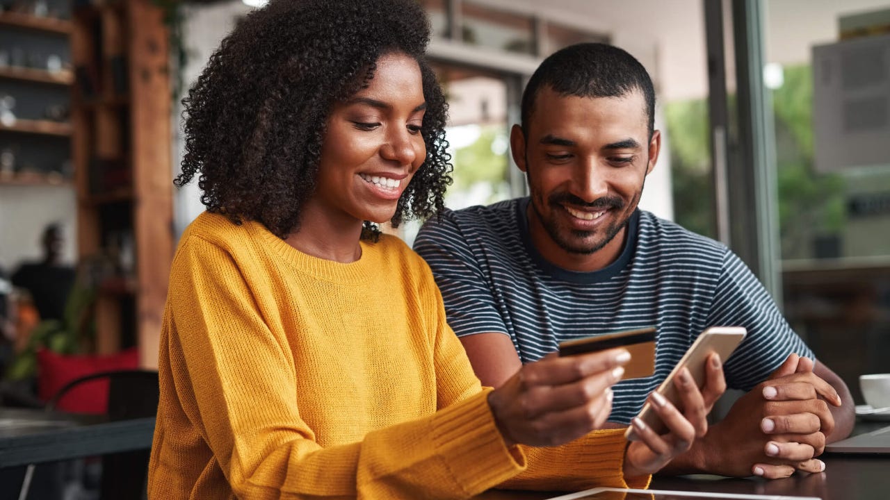 Young woman uses smartphone and smiles with credit card in hand with a young man