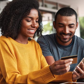Young woman uses smartphone and smiles with credit card in hand with a young man
