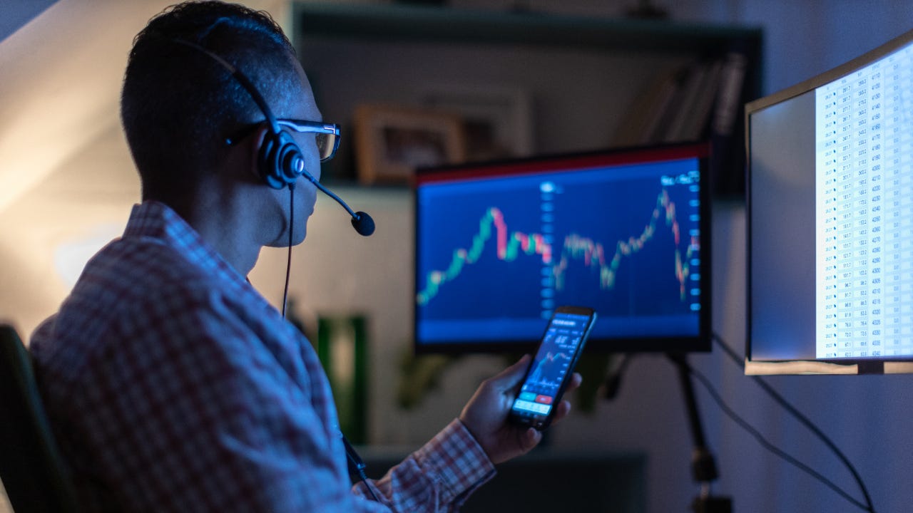 A man looks at his phone and computer screen while trading