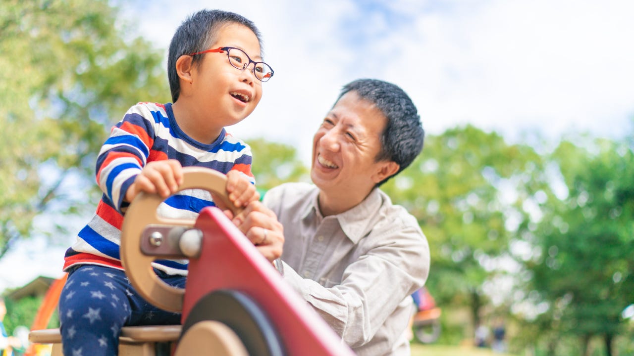 Child with down syndrome enjoying with his father at public park