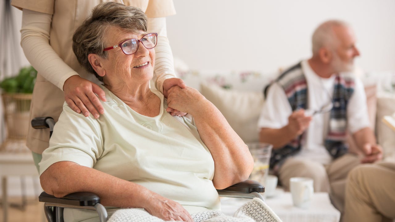 Happy senior lady sitting at wheelchair in nursing home for elderly