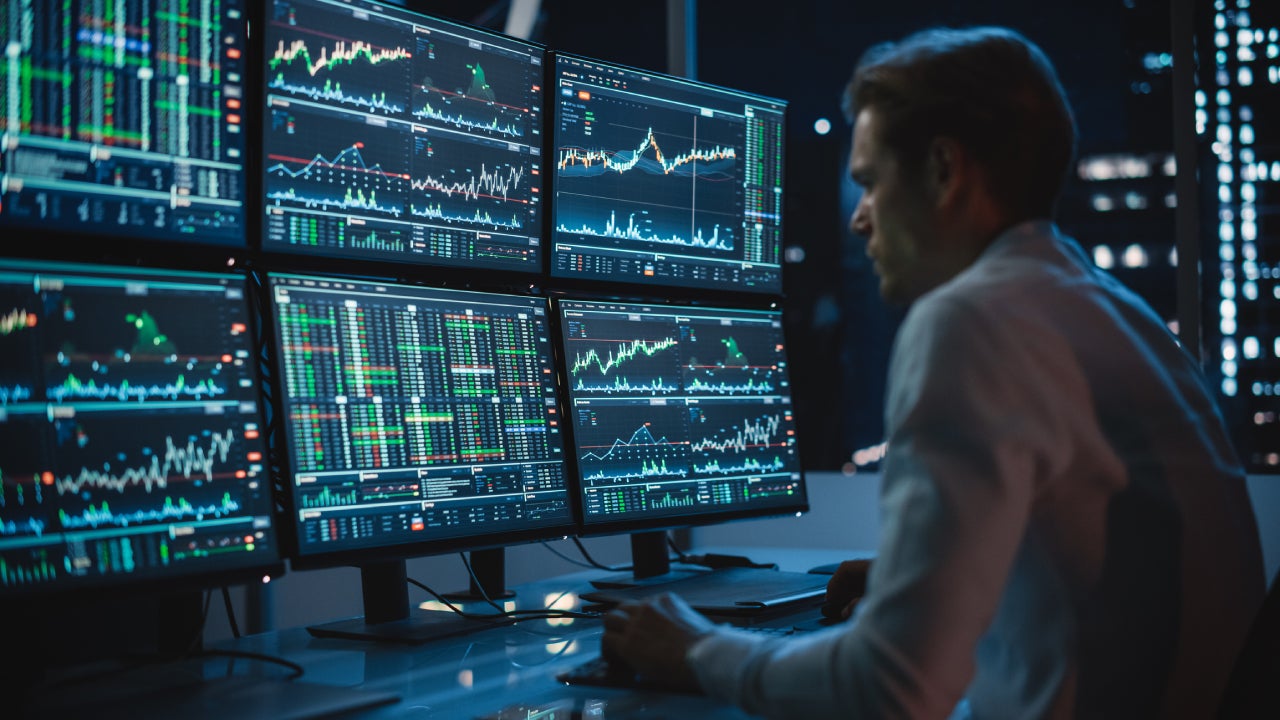 Financial Analyst Working on a Computer with Multi-Monitor Workstation with Real-Time Stocks