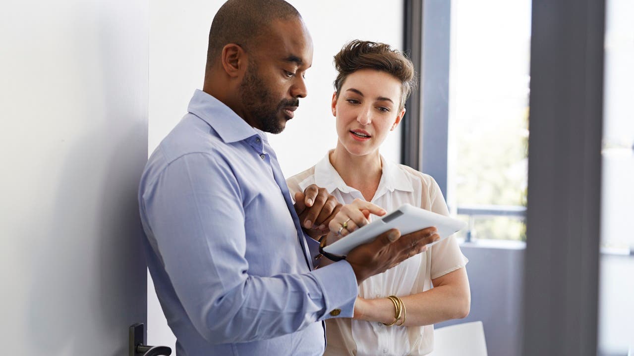 Black man and white woman look at a tablet together.