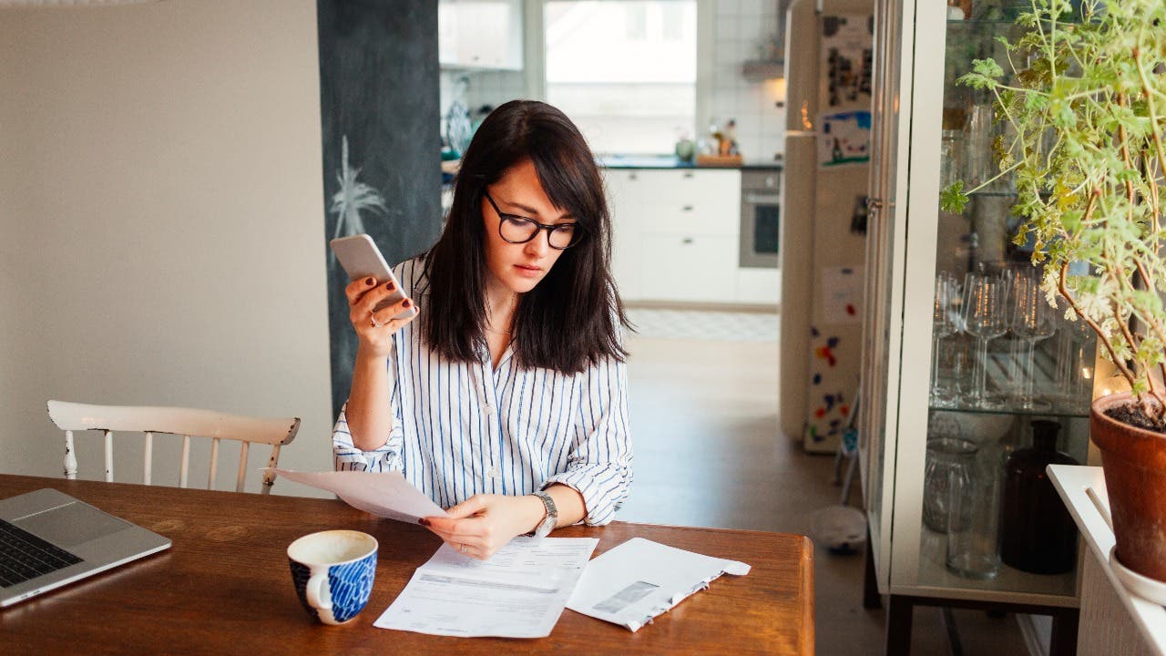 Woman looks through bills at a kitchen table