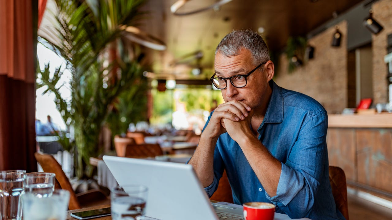 A businessman sits at a table with his laptop