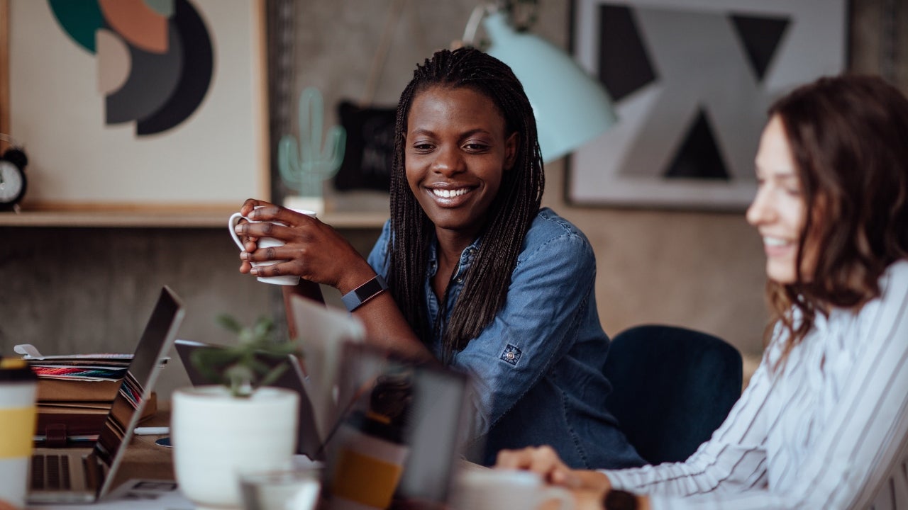 Woman holds a cup of coffee and looks at a computer