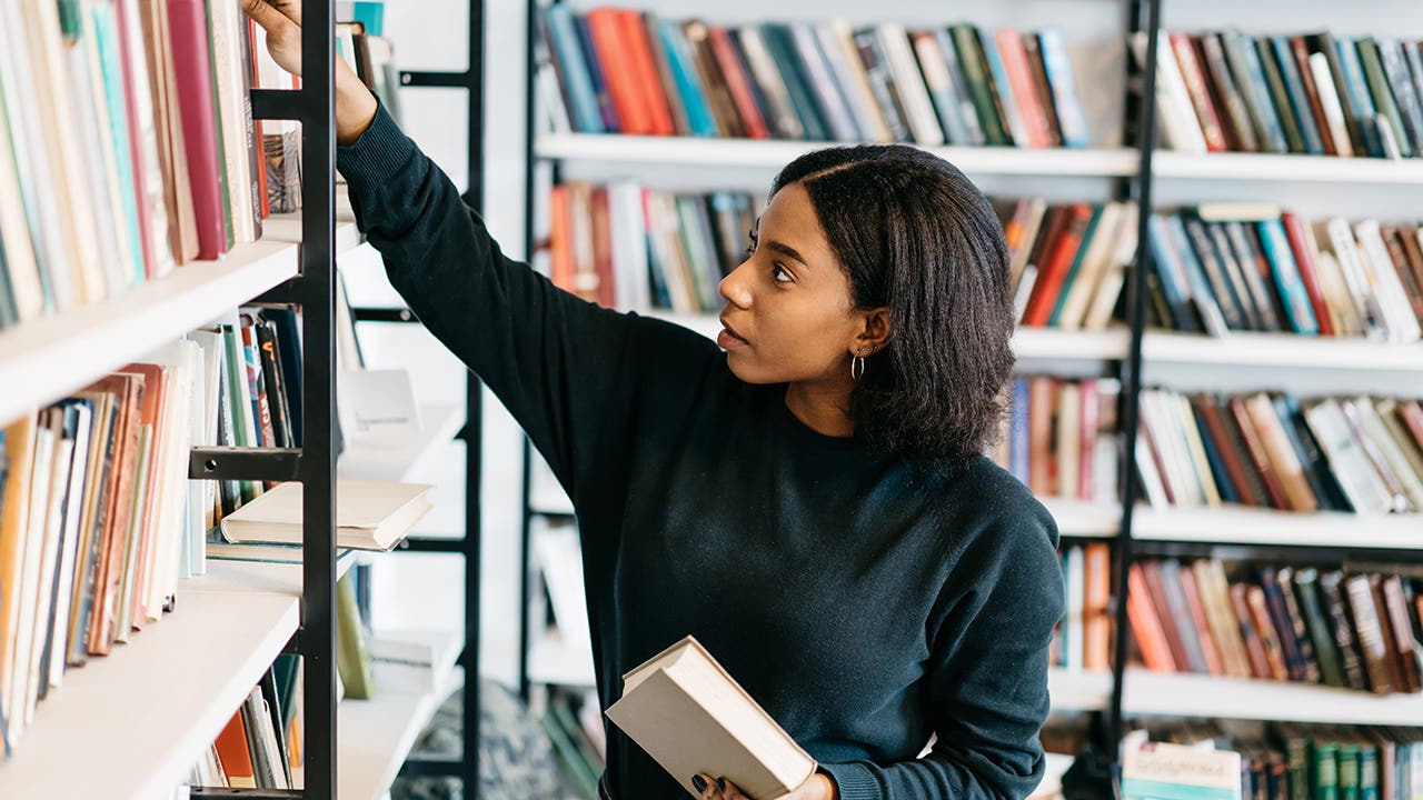 Young female african american librarian making order on bookshel