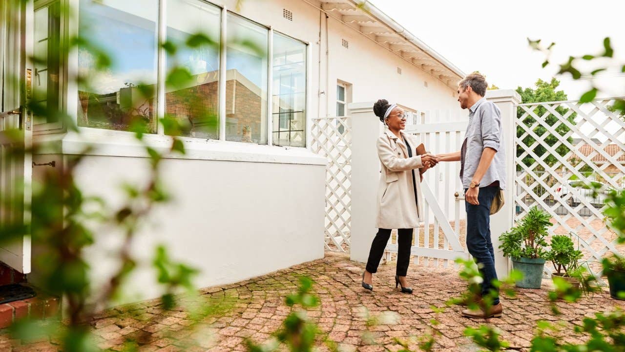 Two people shaking hands in front of a house