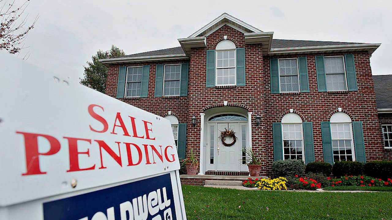 A Coldwell Banker "sale pending" sign outside of a colonial style red brick home with green shutters