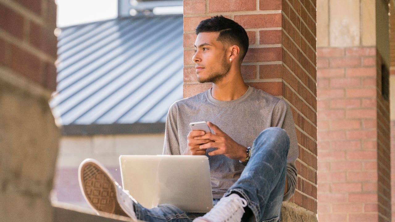 College student sits outside with laptop and cellphone