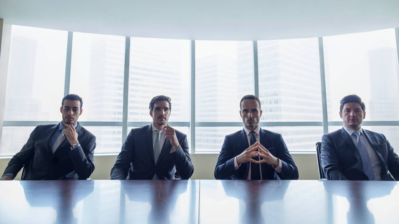 Row of stern businessmen sitting at conference table