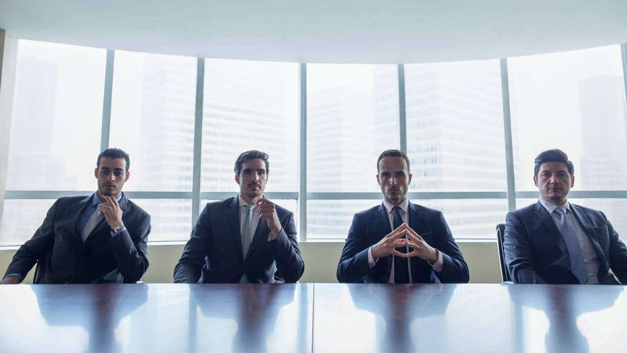 Row of stern businessmen sitting at conference table