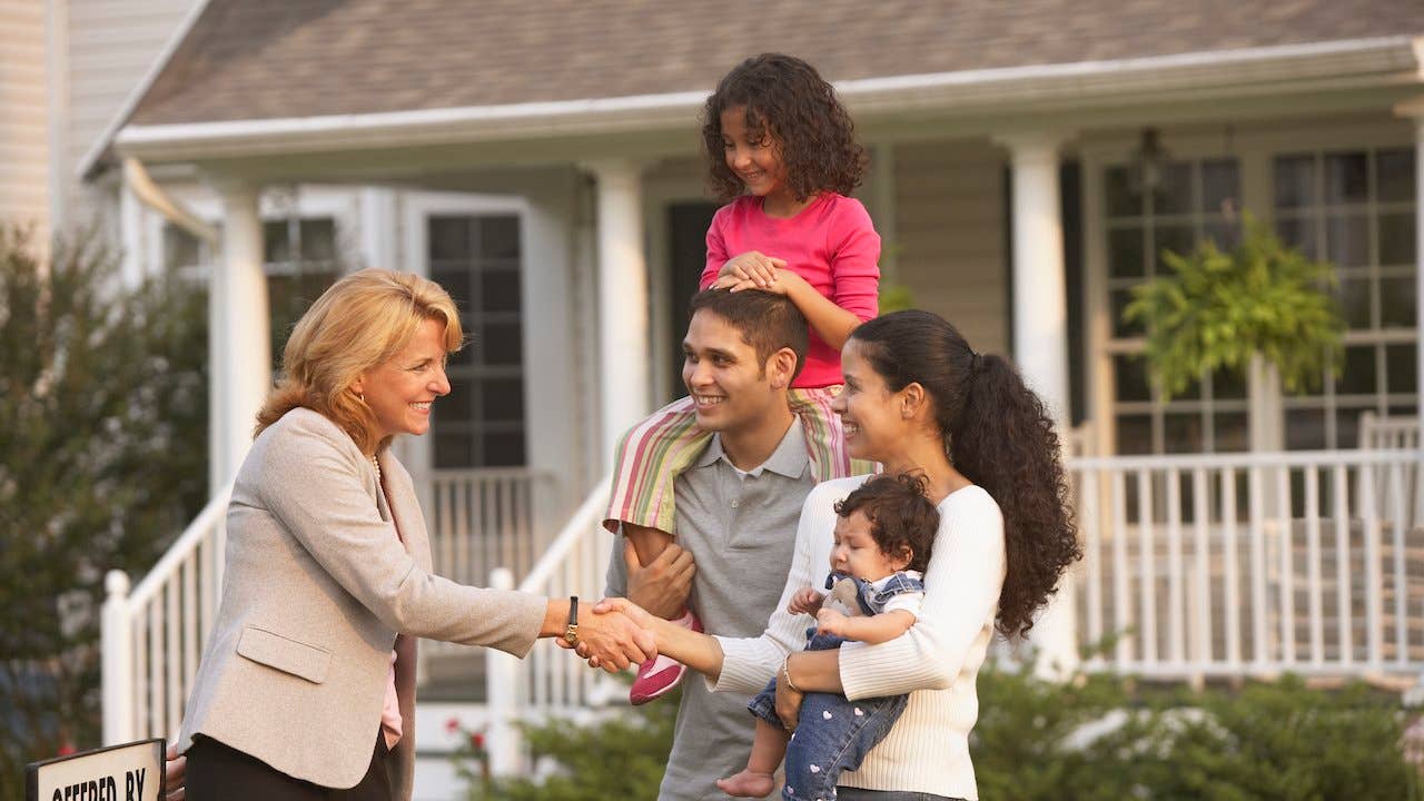 A young family meets with a realtor outside a home with a for sale sign outside