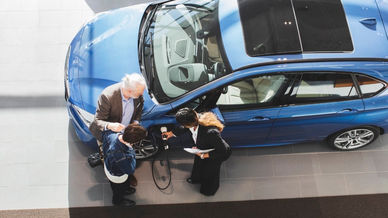 Saleswoman explaining customers to charge electric car at showroom