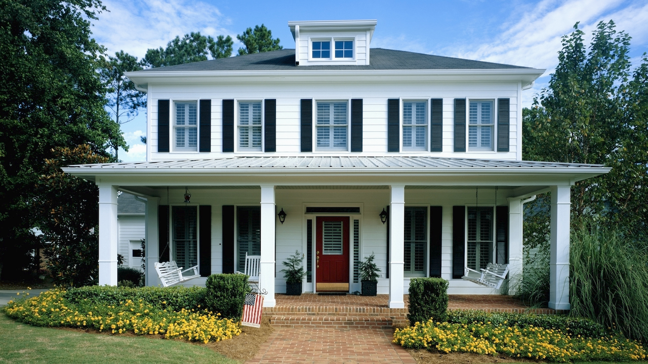 white home with flowerbeds, brick walkway and front porch with rocking chairs
