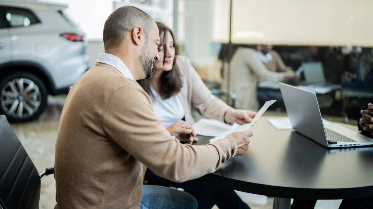 A white man and woman sit together and review paperwork at a dealership.