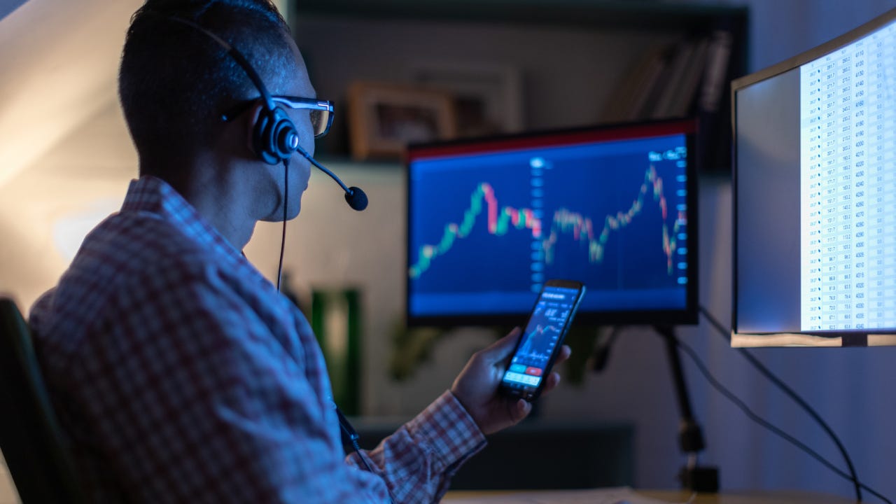 Man looking at currency trading app on his smart phone from his home office