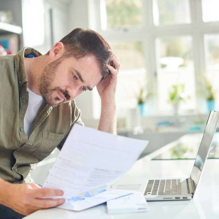 Man reviewing finances over kitchen counter with wife and child in the background.