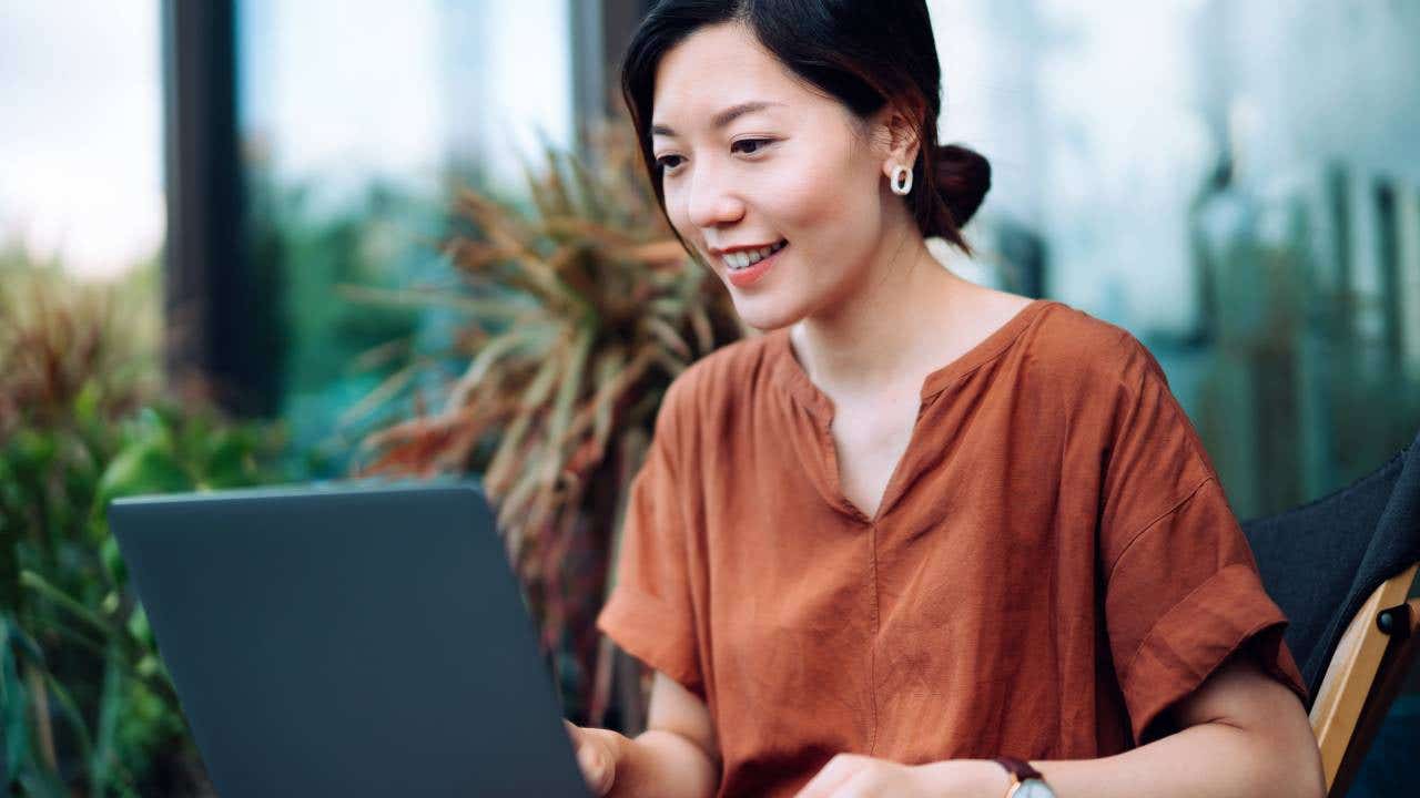 Young Asian woman using a laptop while seated on a balcony.