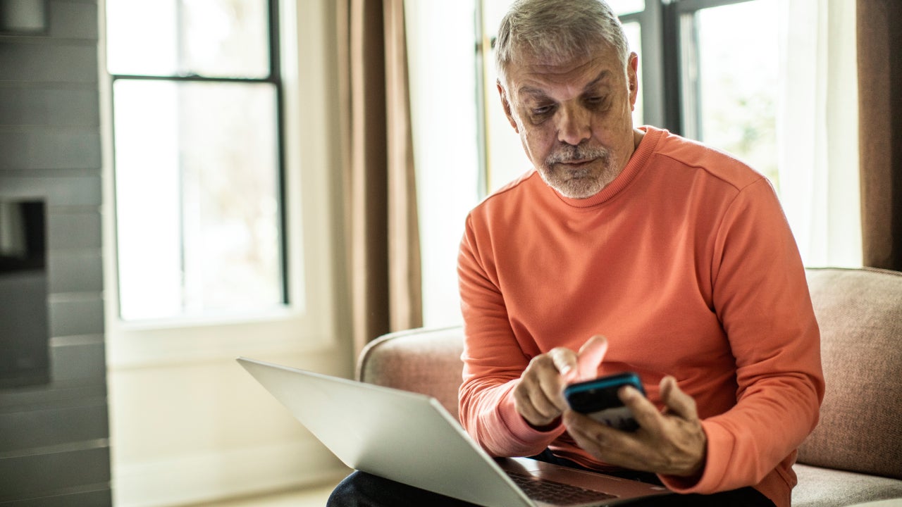 Older man using laptop computer and smartphone at home.