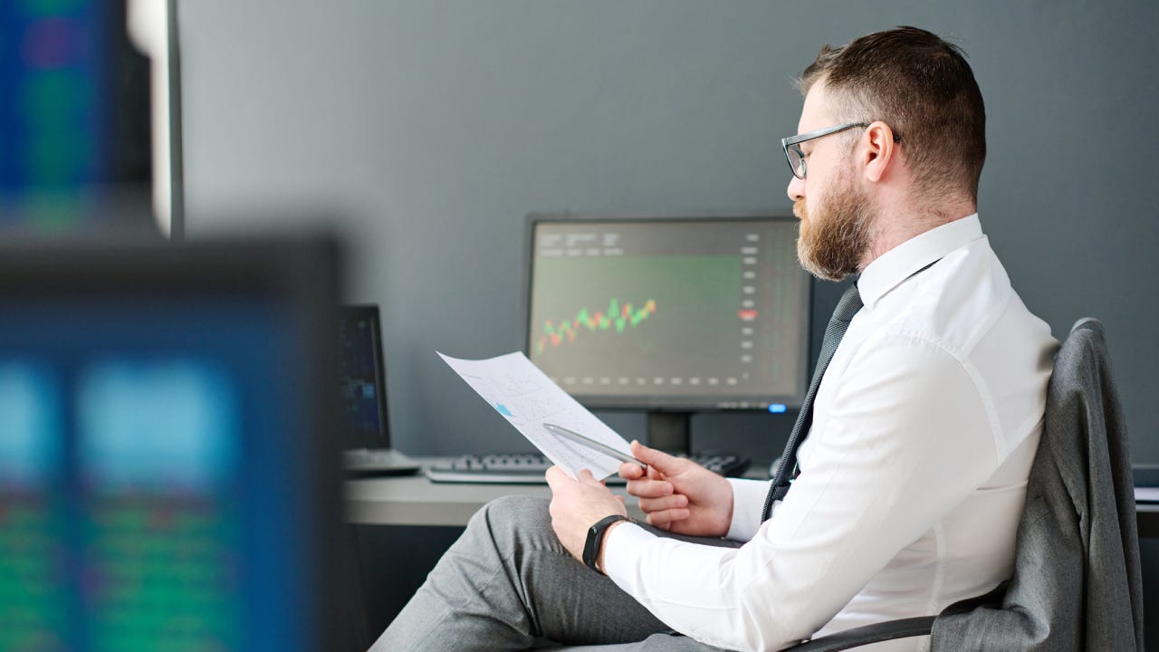Young adult man with beard on face sitting at desk in office working on investment business strategy