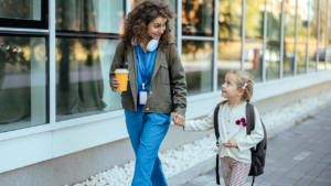 Girl with backpack holding her mother's hand and going to school.