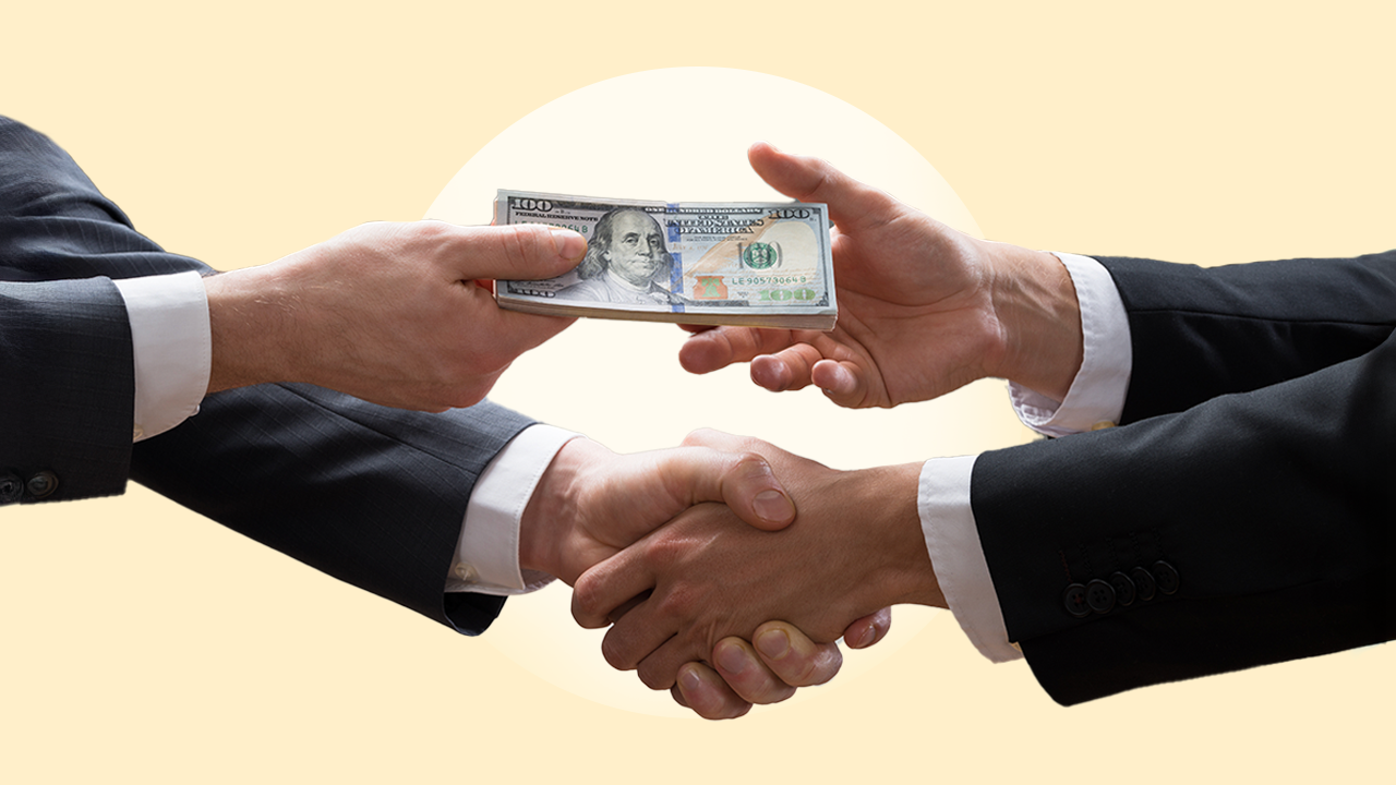 close up of two businesspeople shaking hands and exchanging a stack of $100 bills