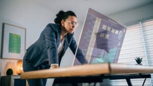 A businesswoman watches a screen showing a downward trending chart.