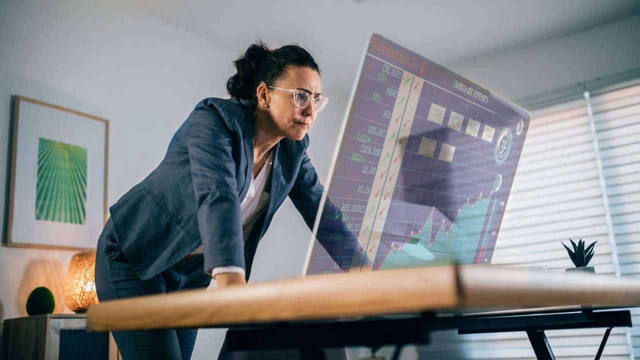 A businesswoman watches a screen showing a downward trending chart.