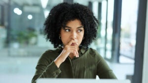 A young businesswoman looking thoughtful while using a laptop in a modern office