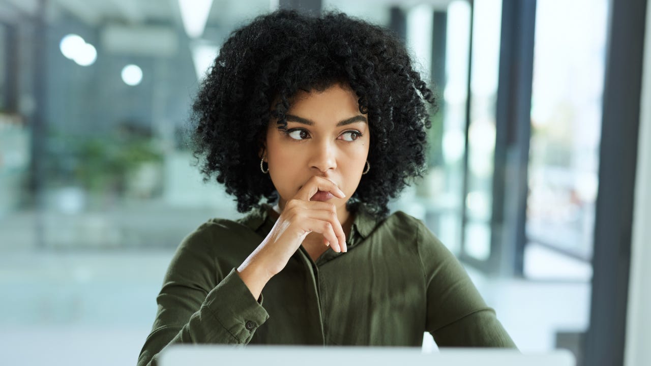 A young businesswoman looking thoughtful while using a laptop in a modern office