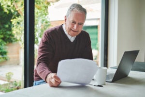 Elderly man looking at his insurance policy sitting next to an open laptop