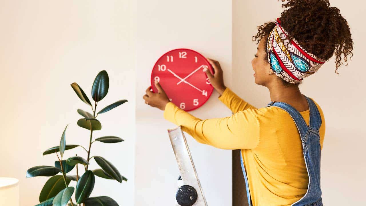 A woman hangs a red clock on her wall.