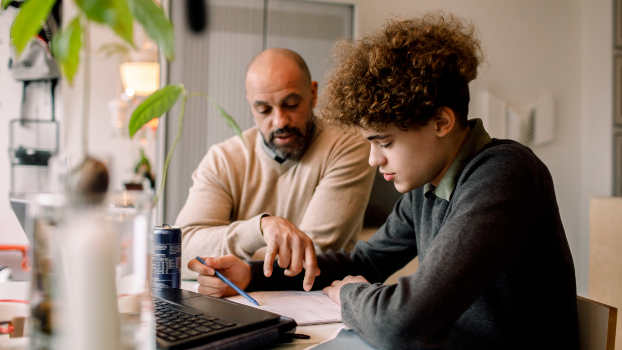 Father guiding son doing homework while sitting at table.