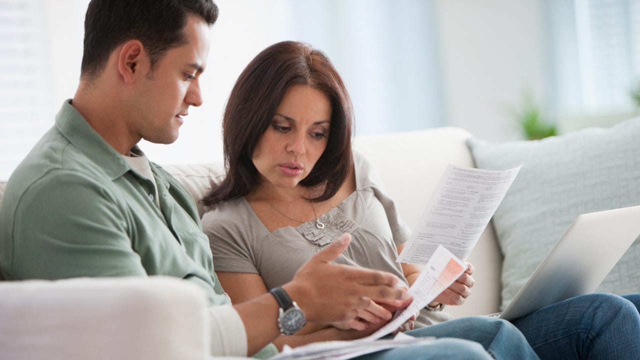 Male and female couple sit on couch and review finances.