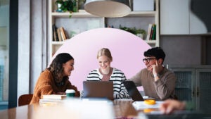 Three colleagues sitting and working together around a laptop.