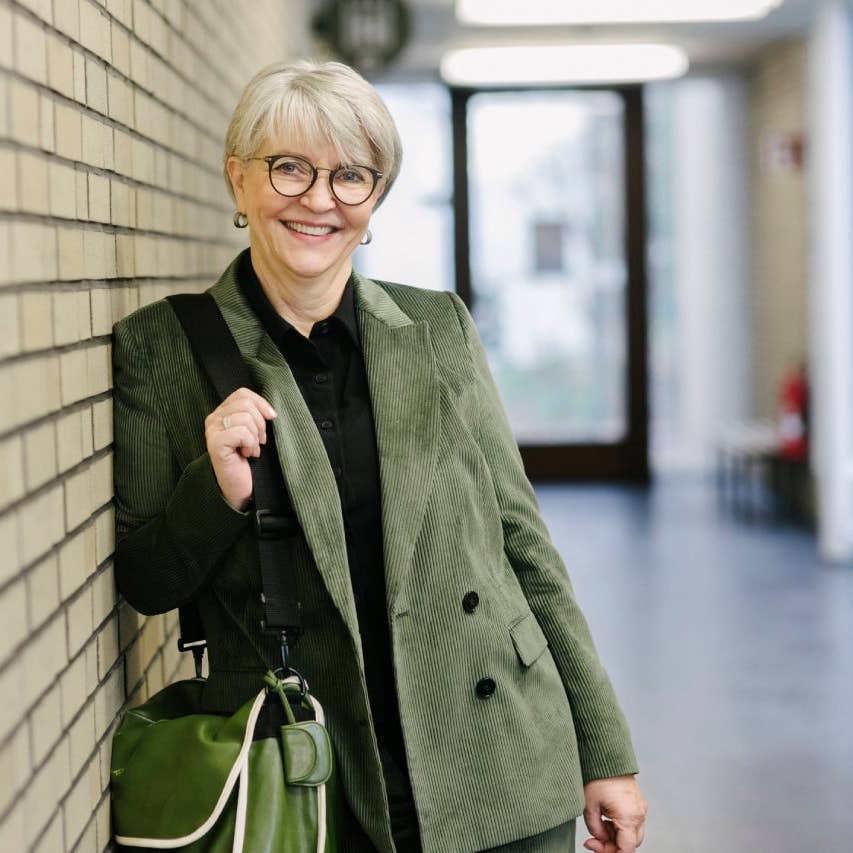 A portrait of a mature school tutor smiling while leaning on a brick wall in a school hallway.