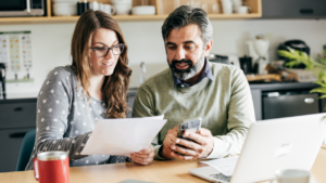 A couple reviews tax paperwork, with their laptop open, while at their kitchen table.