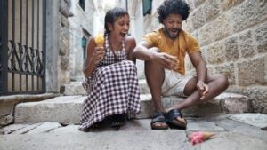 A young man with his girlfriend laughing while seeing fallen ice cream on steps in alley during vacation.