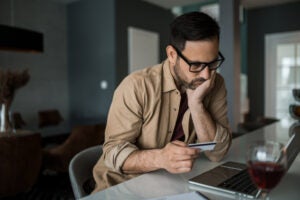 Young entrepreneur paying online with credit card on his laptop at home and going bankrupt.