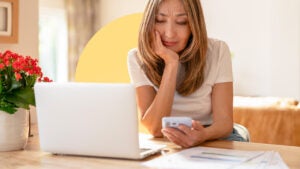 A woman sitting at a table with her laptop open, looking at a calculator in her hand.