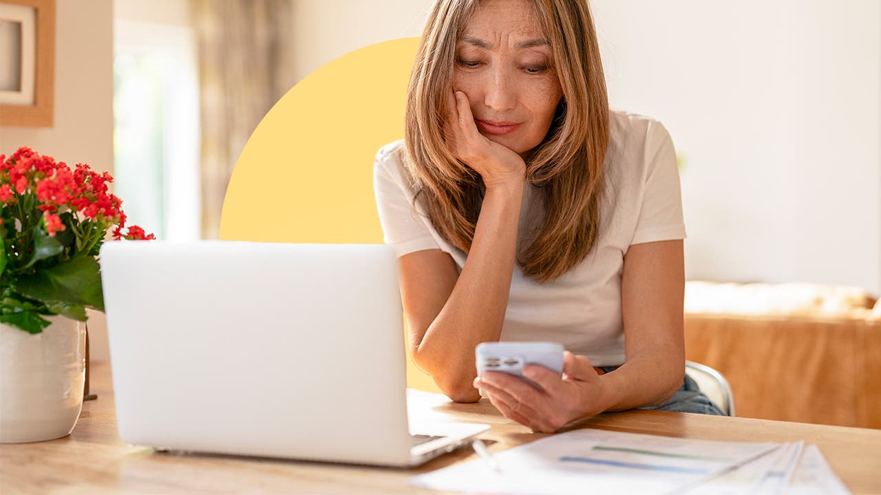 A woman sitting at a table with her laptop open, looking at a calculator in her hand.