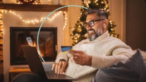 Smiling older man sitting in a living room. He uses a laptop while holding a credit card.