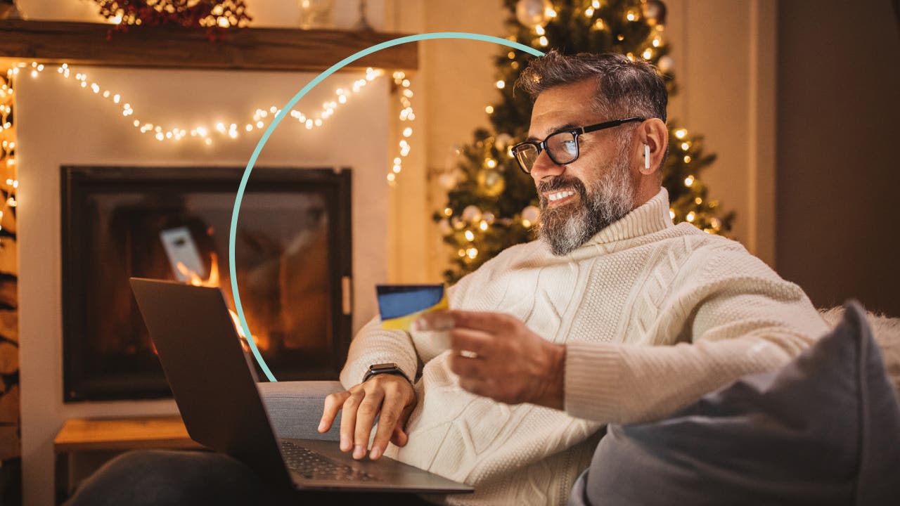 Smiling older man sitting in a living room. He uses a laptop while holding a credit card.