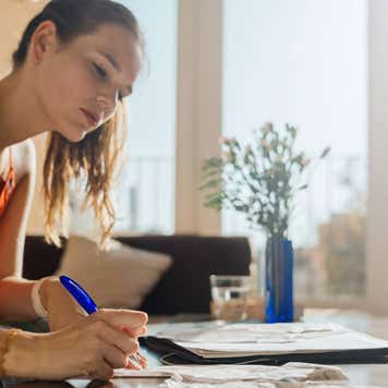 A woman works on her financial accounts at home on a sunny afternoon.
